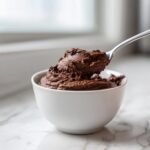 A spoonful of rich, dark chocolate mousse being lifted from a white bowl, perfect for a 5 Minute Keto Chocolate Mousse Delight.