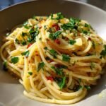Close-up of a bowl of spaghetti Aglio e Olio, a classic Italian pasta recipe, garnished with fresh parsley and chili flakes.