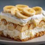 A slice of creamy banana pudding recipe layered with vanilla wafers and fresh banana slices, topped with whipped cream.
