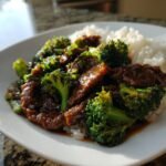 A plate of steaming beef and broccoli recipe served over white rice, glistening with savory sauce.