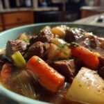 Close-up of a steaming bowl of beef stew recipe, featuring tender chunks of beef, carrots, potatoes, and celery in a rich broth.