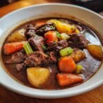 A close-up of a hearty bowl of beef stew recipe, featuring tender chunks of beef, carrots, potatoes, and celery in a rich broth.