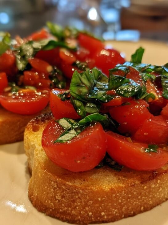 Close-up of two slices of toasted bread topped with fresh tomatoes and basil for a bruschetta recipe.