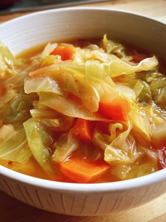 A close-up of a white bowl filled with a hearty cabbage soup recipe, featuring tender cabbage and carrots in a flavorful broth.