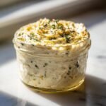 A close-up of a jar filled with creamy homemade Caesar dressing recipe, garnished with herbs.