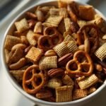 A close-up overhead view of a white bowl filled with a crunchy homemade chex mix recipe, featuring pretzels, nuts, and chex cereal.
