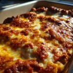 Close-up of a bubbly, golden-brown cheese topping on a chicken enchilada recipe in a baking dish.