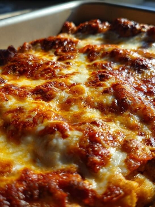 Close-up of a bubbly, golden-brown cheese topping on a chicken enchilada recipe in a baking dish.