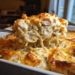 A serving spoon lifts a generous portion of creamy chicken spaghetti recipe casserole, showing melted cheese and tender chicken.