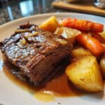 A close-up of a slice of tender chuck roast recipe served with roasted potatoes and carrots in a rich gravy.