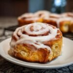 Close-up of a freshly baked cinnamon roll recipe with gooey cream cheese frosting.