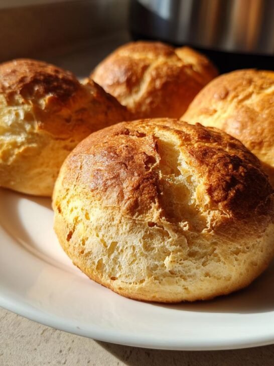 Close-up of four golden-brown cottage cheese buns arranged on a white plate, ready to be enjoyed.