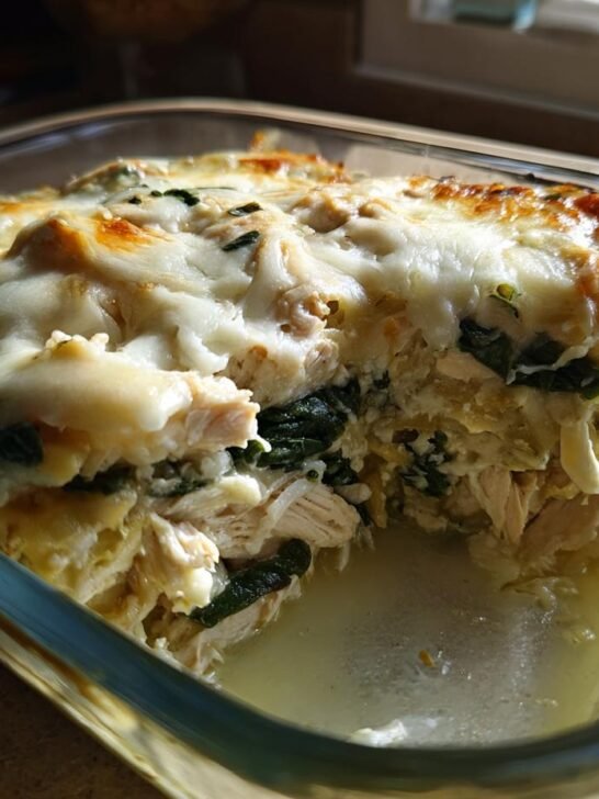 Close-up of a Creamy High Protein Spinach Artichoke Chicken Casserole in a glass baking dish, with melted cheese.
