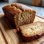 A slice of moist and delicious banana bread on a wooden cutting board.