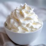 A close-up of a white bowl filled with fluffy, freshly made whipped cream from our easy whipped cream recipe.