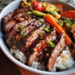 Close-up of a flavorful steak bowl, featuring sliced steak over rice with mixed vegetables and a glossy sauce.