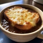 A close-up of a bowl of French Onion Soup Recipe topped with a golden-brown, melted cheese crouton.