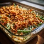A close-up, angled view of a freshly baked green bean casserole recipe in a glass baking dish, topped with crispy fried onions.
