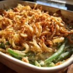 Close-up of a classic green bean casserole recipe, topped with crispy fried onions in a white baking dish.
