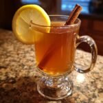 A steaming mug of hot toddy recipe, garnished with a lemon slice and a cinnamon stick.