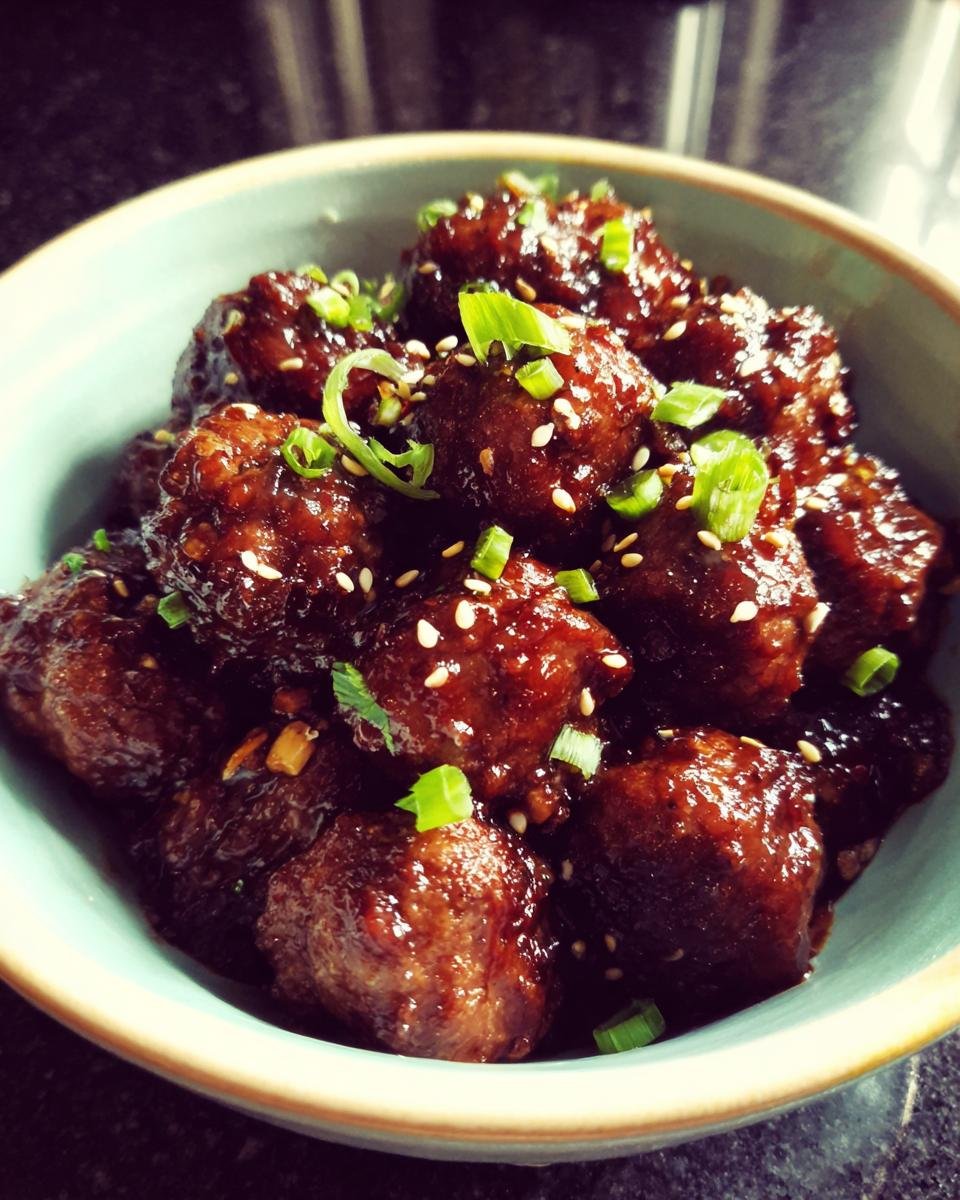 Close-up of Irresistible Asian Crockpot Meatballs glazed in a rich sauce, garnished with sesame seeds and green onions.