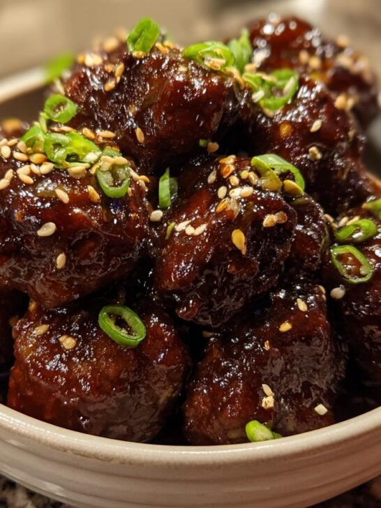 Close-up of Irresistible Asian Crockpot Meatballs glazed in a dark sauce, garnished with sesame seeds and chopped green onions.