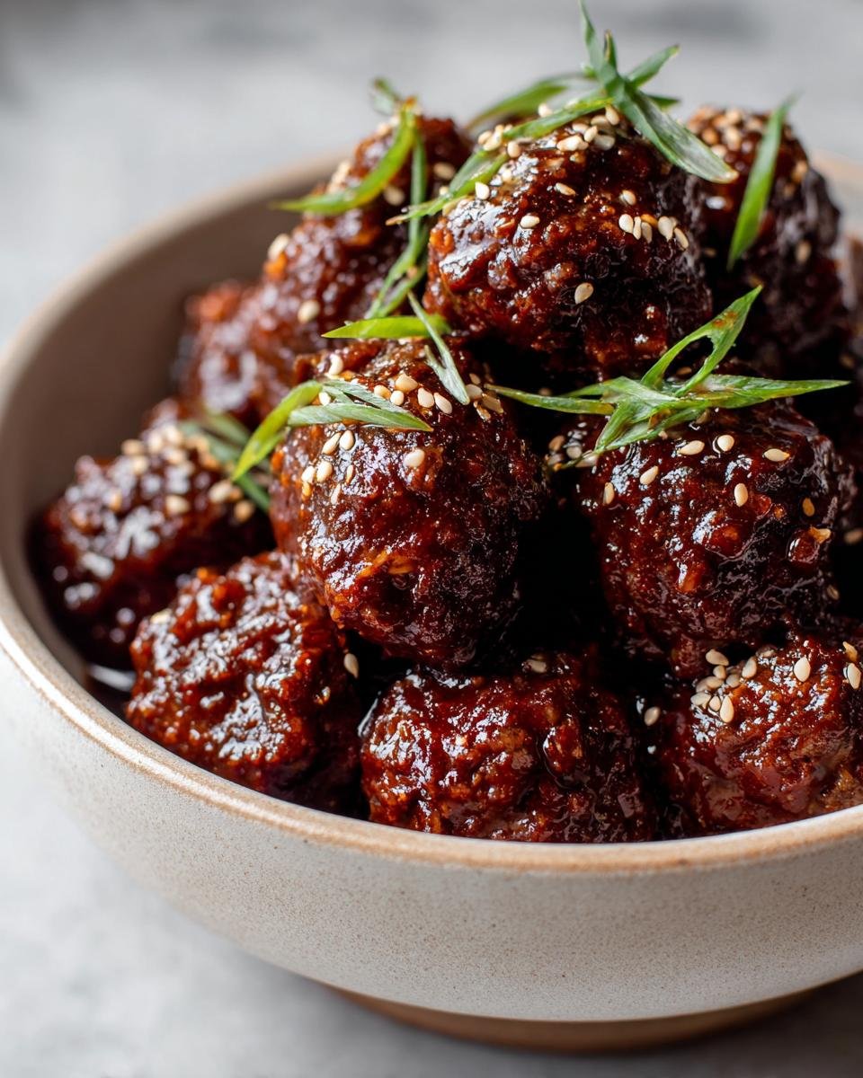 Close-up of Irresistible Asian Crockpot Meatballs glazed in a rich sauce, sprinkled with sesame seeds and green onions.