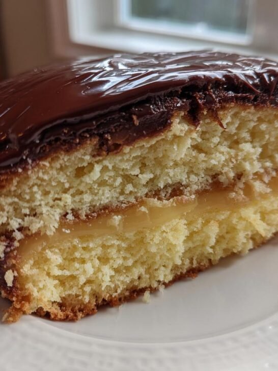A delicious slice of Irresistible Boston Cream Pie, showcasing layers of yellow cake, creamy custard, and rich chocolate ganache.