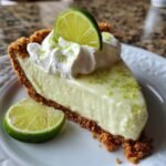 A slice of key lime pie with whipped cream and lime zest, garnished with a lime wedge.