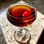 A perfectly chilled Manhattan recipe cocktail in a coupe glass, garnished with a bright red cherry.