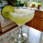 A refreshing margarita recipe in a salt-rimmed glass, garnished with a lime wedge.