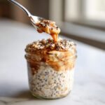A close-up of a jar filled with overnight oats, topped with nuts, seeds, and a drizzle of caramel sauce.