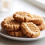 A close-up of a stack of freshly baked peanut butter cookies with classic fork marks.