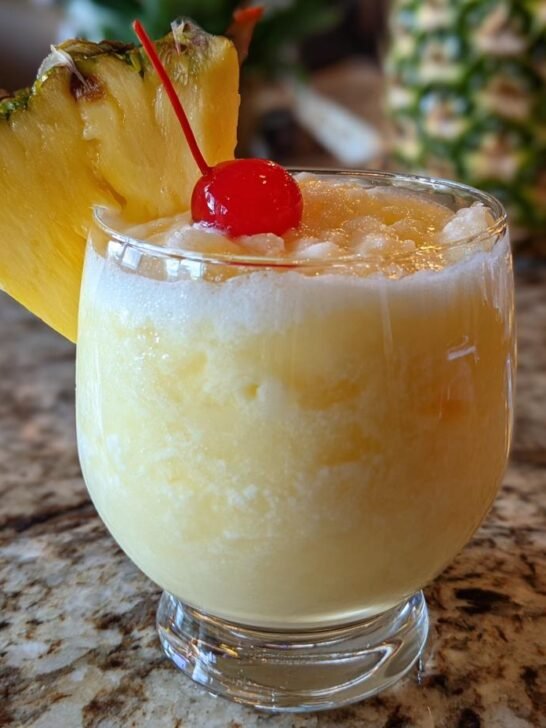 A delicious frozen pina colada recipe drink garnished with a pineapple wedge and a maraschino cherry.