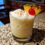 A delicious frozen pina colada recipe drink in a glass, garnished with pineapple and a cherry.