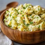 Close-up of a creamy potato salad recipe in a wooden bowl, garnished with chives and bacon bits.