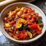 A close-up of a rustic bowl filled with a vibrant ratatouille recipe, showcasing tender zucchini, eggplant, bell peppers, and tomatoes.