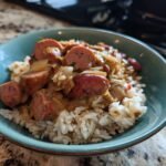 A close-up of a bowl of red beans and rice recipe, featuring tender red beans, fluffy white rice, and sliced sausage.
