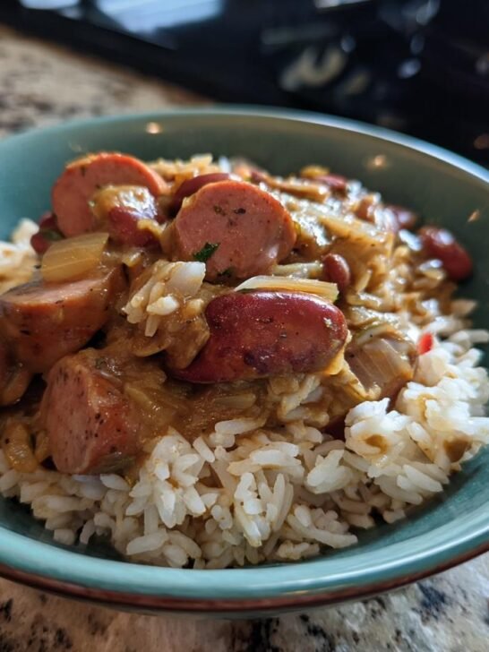 A close-up of a bowl of red beans and rice recipe, featuring tender red beans, fluffy white rice, and sliced sausage.