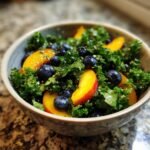 A bowl of refreshing summer peach and blueberry kale salad, showcasing vibrant colors and fresh ingredients.