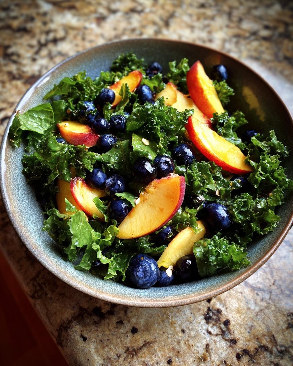 A bowl of Refreshing Summer Peach and Blueberry Kale Salad, showcasing vibrant kale, sliced peaches, and plump blueberries.