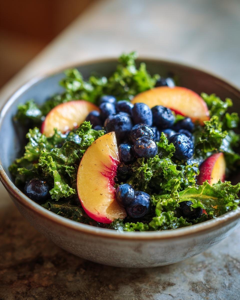 A close-up of a Refreshing Summer Peach and Blueberry Kale Salad in a bowl, featuring fresh kale, sliced peaches, and blueberries.