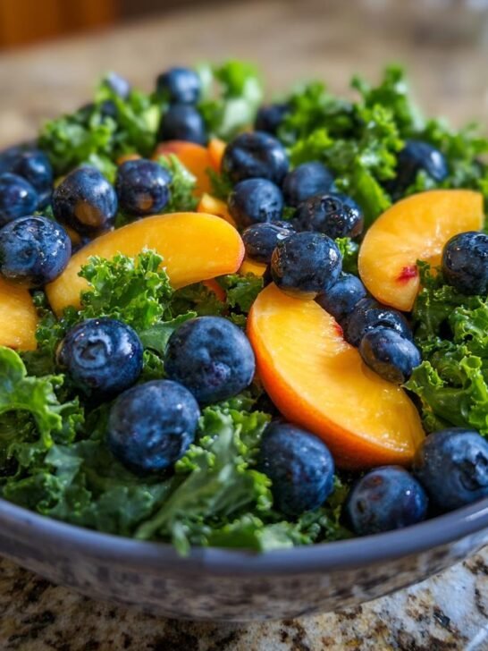 A close-up of a Refreshing Summer Peach and Blueberry Kale Salad in a blue bowl, showcasing vibrant blueberries and sliced peaches on a bed of kale.