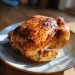 A perfectly roasted whole rotisserie chicken with crispy, golden-brown skin sits on a plate.