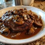 A juicy Salisbury steak recipe served with a rich mushroom and onion gravy on a white plate.