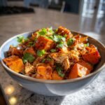 Close-up of a bowl filled with shredded BBQ chicken and roasted sweet potato cubes, garnished with fresh cilantro.