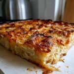 A close-up of a golden-brown slice of scalloped potatoes recipe, showing layers of thinly sliced potatoes and creamy sauce.