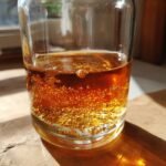 Close-up of a glass jar filled with amber-colored simple syrup, showing small bubbles rising.