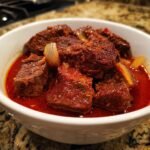 A close-up of tender beef chunks in a rich, red sauce with onions, showcasing the delicious goulash recipe.