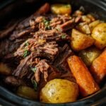 Close-up of a slow cooker recipe featuring tender pot roast with potatoes and carrots, garnished with herbs.